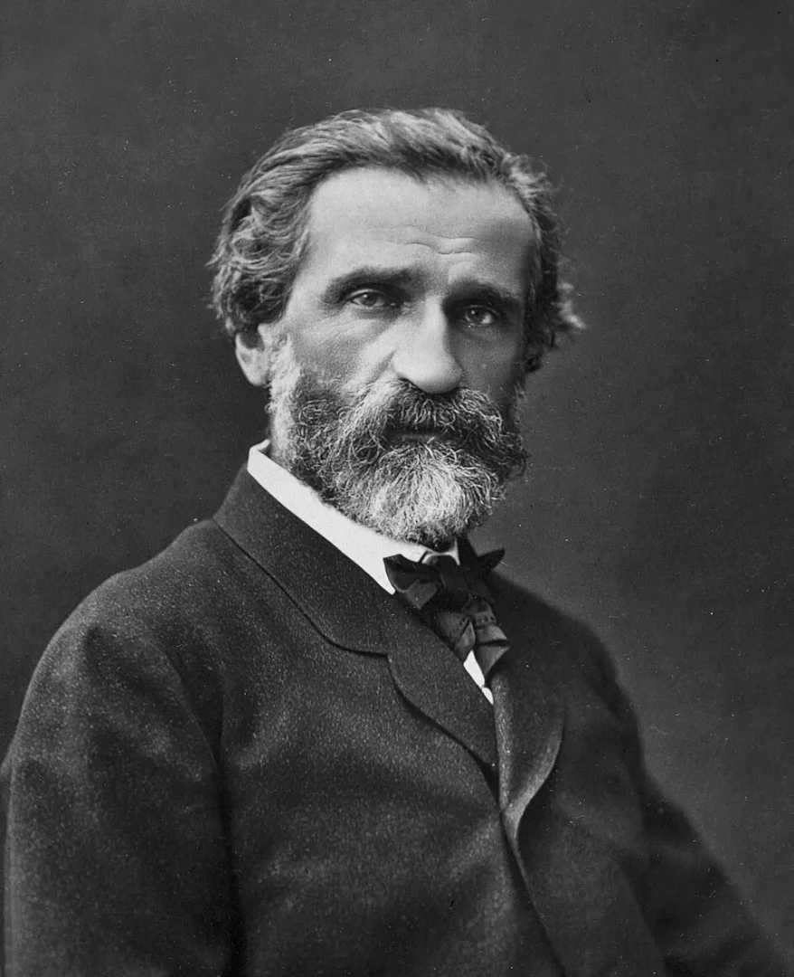 Siyah beyaz portrede, gür beyaz sakalları ve dalgalı saçlarıyla, koyu bir takım elbise ve papyon giyen İtalyan opera bestecisi Giuseppe Verdi, belirgin bir ifadeyle doğrudan kameraya bakıyor.