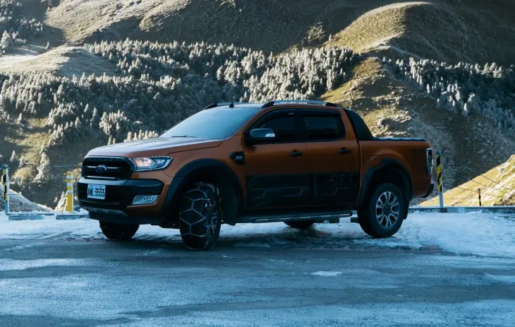 Kar zinciri takılı pick-up aracın karlı dağ yolunda park halinde görüntüsü; kış sürüşü ve zorlu koşullarda araç güvenliği
