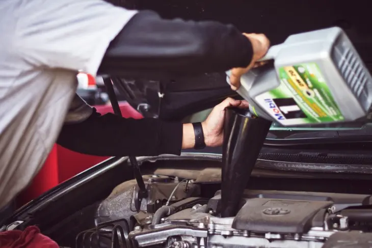 Bir kişinin araca motor yağı eklemesi; kış ayları için düşük viskoziteli motor yağı değişimi
