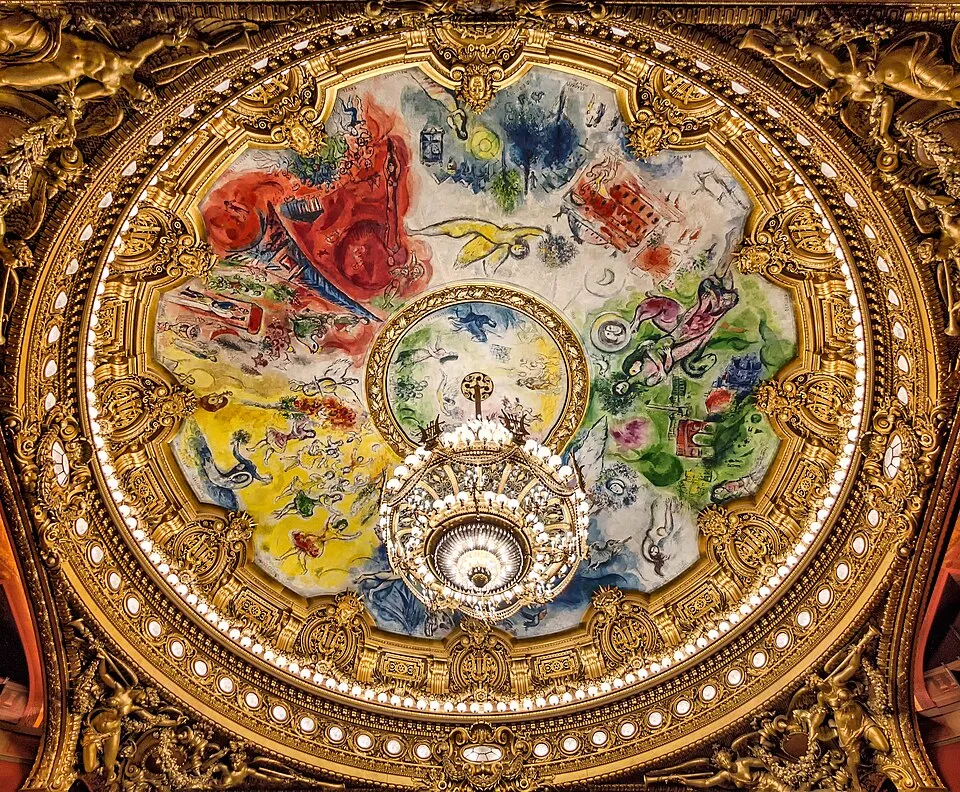 Paris'teki ünlü Palais Garnier opera binasının tavanında yer alan, ortasında büyük ve gösterişli bir avizenin sarktığı, Marc Chagall'ın rengarenk, rüya gibi figürler ve müziğe adanmış sahneler içeren dairesel fresk tablosu, etrafı altın yaldızlı detaylı mimari süslemelerle çevrili büyüleyici bir görüntü sunuyor.