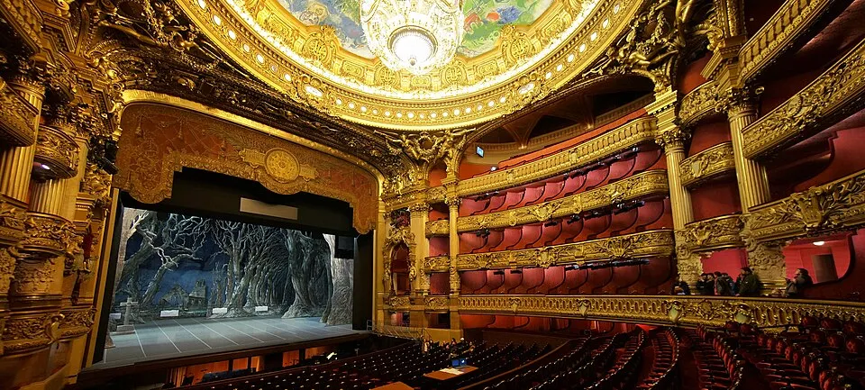 Paris'teki görkemli Palais Garnier Opera Binası'nın, altın varaklı süslemelerle bezeli balkonları, kırmızı kadife koltukları ve sahnesinde karanlık bir orman dekorunun yer aldığı, ortasında büyük bir avizenin asılı olduğu Marc Chagall tavan resminin de görüldüğü muazzam iç görünümü.