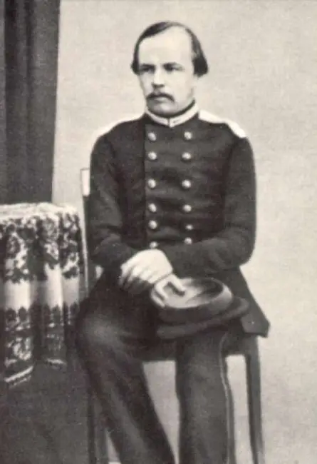 Siyah beyaz eski bir fotoğrafta, askeri üniforması, bıyığı ve hafif seyrek saçlarıyla ciddi bir ifadeyle bir sandalyede oturan genç Dostoyevsky, kucağında koyu renkli bir şapka tutarken, yazarın hayatına dair önemli bir dönemi yansıtan bir anı kareli masanın yanında ölümsüzleştiriyor.