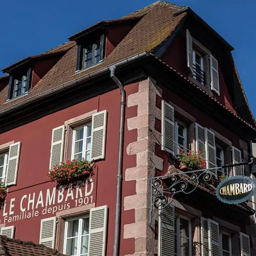 Kaysersberg’de yer alan Le Chambard Hotel’in geleneksel Alsace mimarisiyle tasarlanmış kırmızı cephesi ve çiçekli pencereleri.