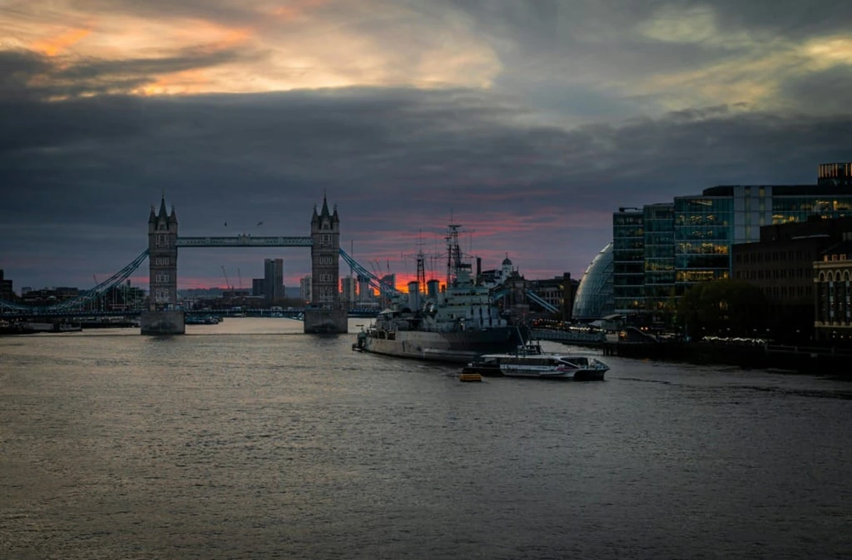 Londra'da gün batımında Thames Nehri üzerinde yükselen tarihi Tower Bridge, önünde demirli HMS Belfast gemisi ve modern yapıların siluetleriyle çevrili bu şehir manzarası, unutulmaz bir seyahat rotası için ilham veriyor.