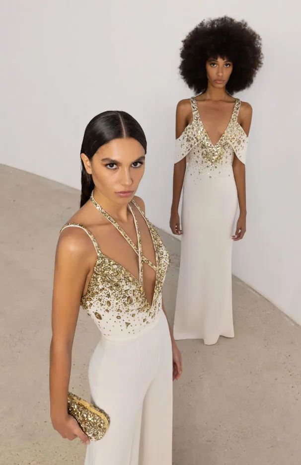 İki modelin beyaz ve altın detaylı ışıltılı yılbaşı elbiseleriyle poz verdiği zarif Zuhair Murad tasarımları.