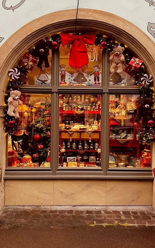Colmar’da Alsace Noel Pazarları döneminde kırmızı ve altın süslemelerle dekore edilmiş yılbaşı temalı mağaza vitrini, oyuncak ayılar ve hediyeliklerle dolu bir Christmas dekorasyonu.