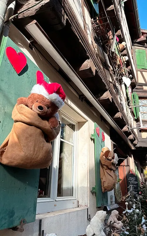 Eguisheim’da Alsace Noel Pazarları döneminde ev cephelerine yerleştirilmiş Noel şapkalı pelüş ayılar ve kırmızı kalplerle süslenmiş yılbaşı dekorları.