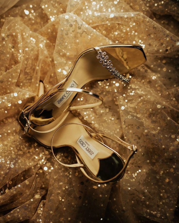 Altın rengi ince bantlı, kristal taş süslemeli Jimmy Choo yüksek topuklu sandalet; ışıltılı tül kumaş üzerinde sergilenen lüks gece ayakkabısı.