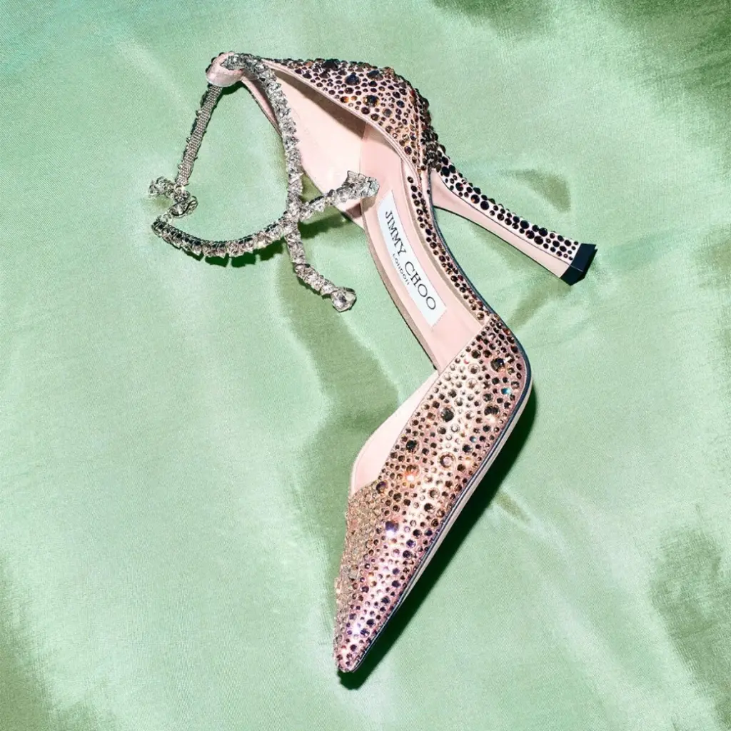 Kristal taşlarla kaplı pembe tonlarında Jimmy Choo stiletto; yeşil saten kumaş üzerinde sergilenen zarif gece ayakkabısı.