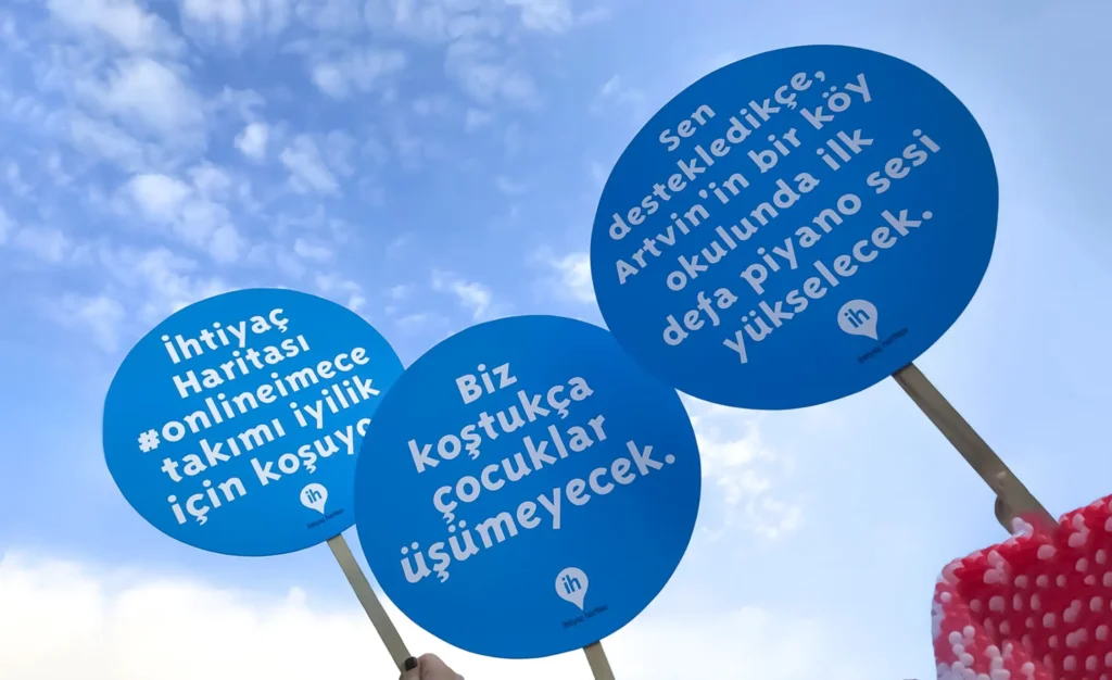İhtiyaç Haritası gönüllülerinin taşıdığı destek mesajı içeren pankartlar – yılbaşında ihtiyaç sahiplerine yardım etmeyi teşvik eden görsel