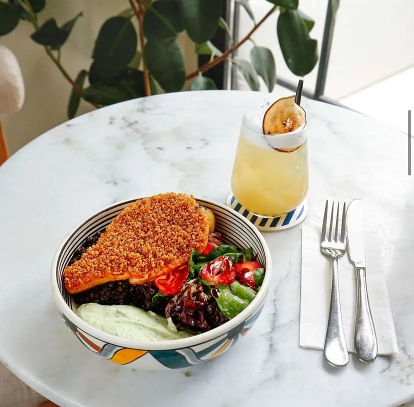 Brokoli, mango, kuru meyveler ve çekirdeklerle süslenmiş, üzerine kremalı sos dökülmüş kase yemeği, yanında yeşil kokteyl — Nişantaşı mekanları rehberinden.