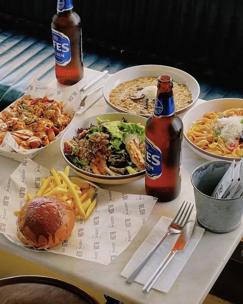 Blok Mekân Bomonti’de burger, makarna, salata ve yanında Efes bira – Silahşör Caddesi’nin canlı atmosferinde keyifli akşam yemeği masası.