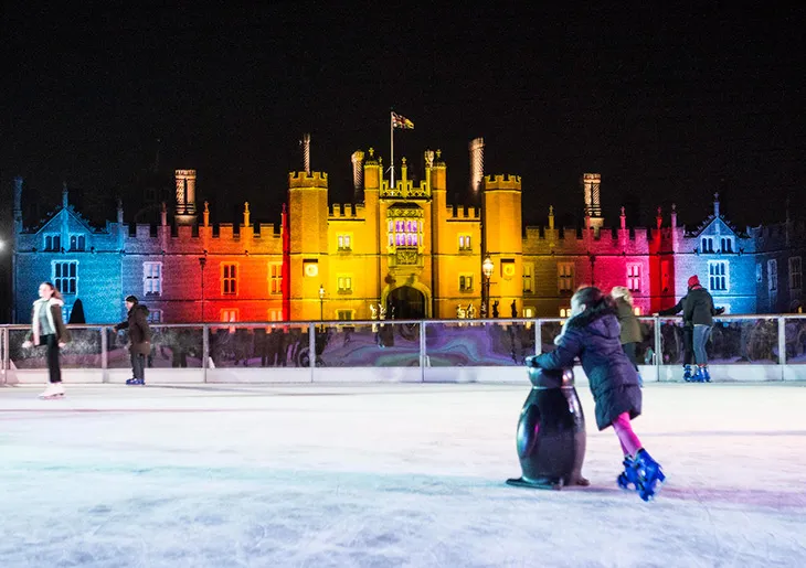Hampton Court Palace önündeki buz pistinde kayan insanlar ve ışıklandırılmış tarihi saray ile Londra’da Noel atmosferi.