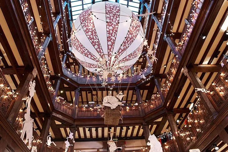 Liberty London mağazasında yılbaşı ışıkları ve sıcak hava balonu temalı Noel dekorasyonlarıyla büyüleyici alışveriş atmosferi.