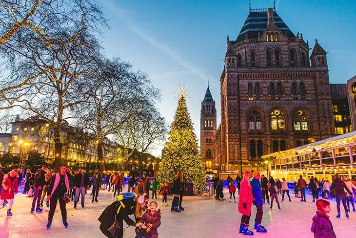 Natural History Museum önünde yılbaşı ağacı ve buz pistinde kayan insanlar ile Londra’da kış ve Noel atmosferi.