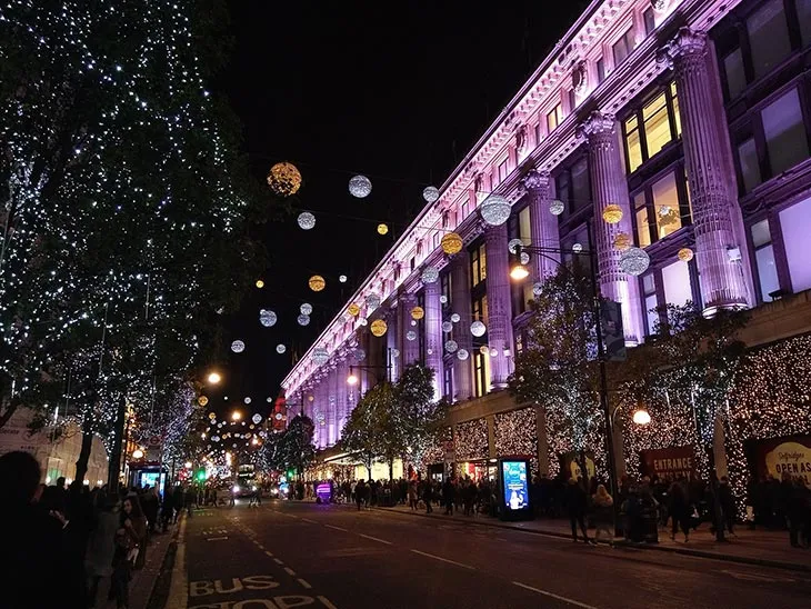 Oxford Street’te Selfridges binasının yılbaşı ışıklarıyla süslenmiş cephesi ve Noel alışverişi yapan kalabalık.