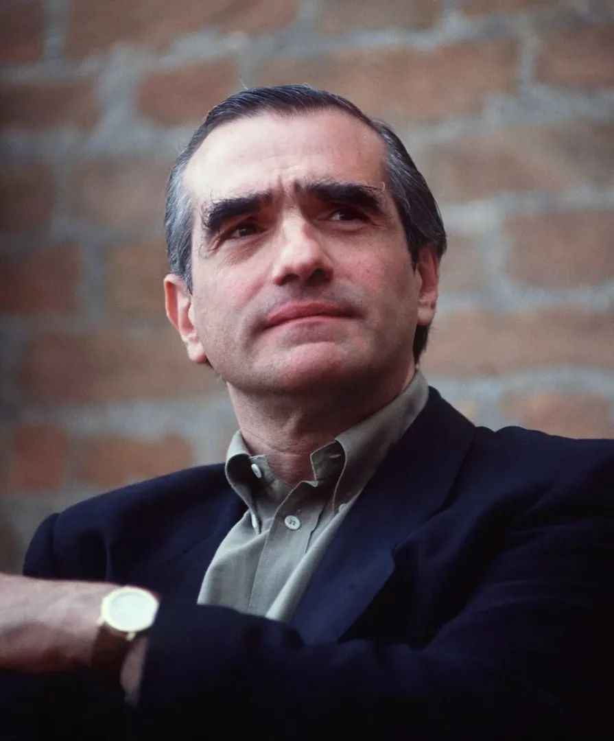 Martin Scorsese'nin hayatı makalesi için, gri saçları, belirgin kaşları ve düşünceli yüz ifadesiyle hafifçe yukarı bakan, koyu renk ceketli ve açık renk gömlekli usta yönetmen Martin Scorsese'nin yakın çekim portresi. Sol bileğinde altın rengi bir saat görülüyor, arka plan bulanık bir tuğla duvardan oluşuyor.