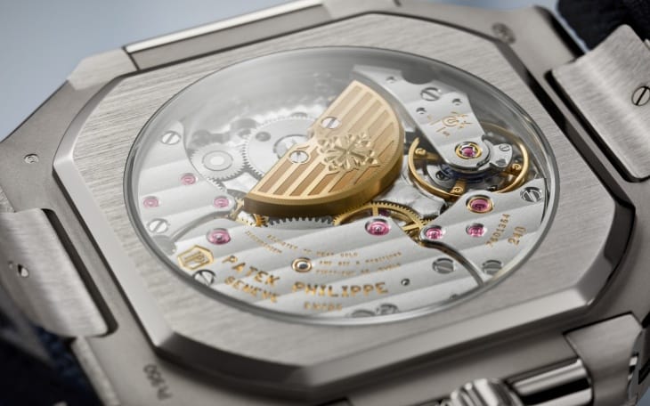 Patek Philippe Cubitus Koleksiyonu'ndan fırçalanmış kasalı bir saatin, içindeki girift çarkları, yakut mücevherleri ve Calatrava armalı altın yarım ay şeklindeki 240 kalibre mekanizmasını gözler önüne seren şeffaf arka kapağı, markanın teknik üstünlüğünü ve yenilikçi ruhunu vurguluyor.