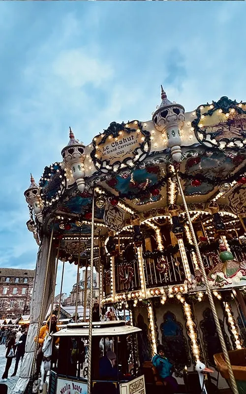 Strasbourg’da Alsace Noel Pazarları sırasında kurulan ışıklı atlı karınca (carousel), süslemeler ve kalabalık yılbaşı atmosferi.