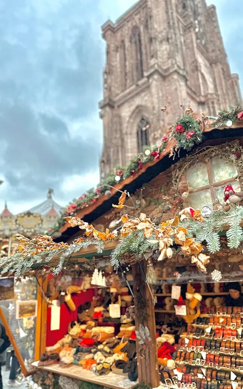 Strasbourg’da Alsace Noel Pazarları sırasında Notre Dame Katedrali’nin yanında yer alan yılbaşı dekorlarıyla süslenmiş ahşap stant ve Christmas pazarı atmosferi.