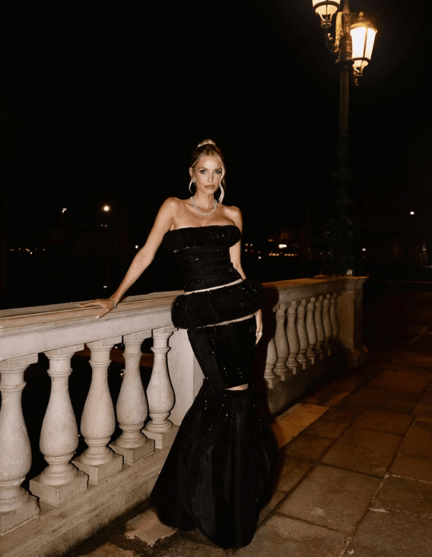 Gece ortamında taş balkonda poz veren straplez siyah couture elbise giymiş şık kadın, zarif takılarıyla yılbaşı ve davet stili ilhamı sunuyor.