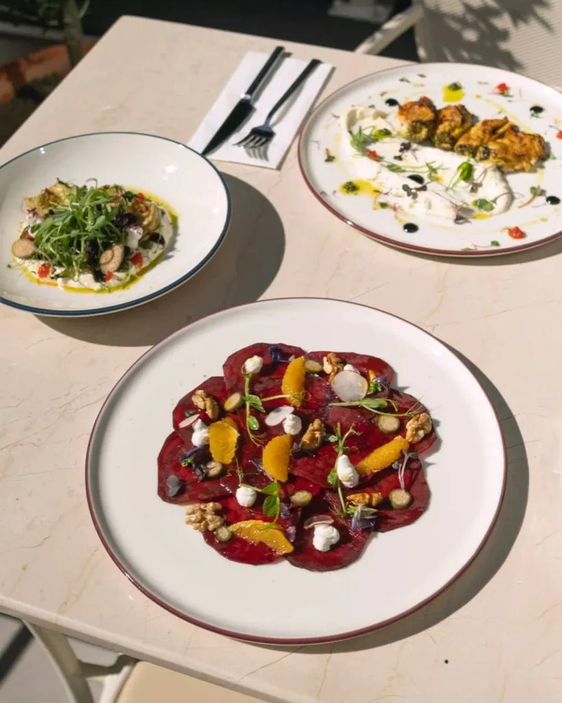 Casa Mamma restoranının davetkar iç mekanında, geleneksel İtalyan lezzetlerini deneyimlemek için beyaz tabaklar ve çatal bıçak takımlarıyla özenle hazırlanmış uzun ahşap masalar, loş ve sıcak aydınlatma, taş duvarlar ve şık bir ambiyans misafirleri bekliyor gibi görünüyor.