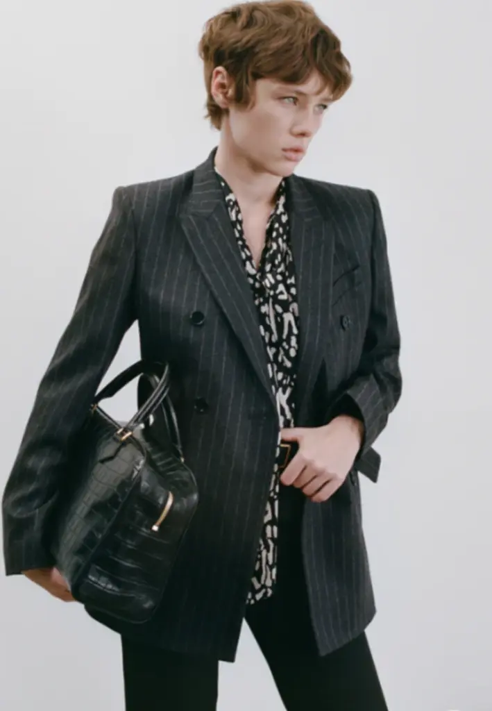 Siyah çizgili blazer ve desenli gömlek kombini, elinde siyah çanta taşıyan model