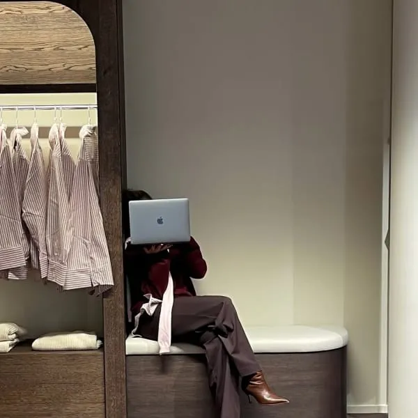 Bordo ceket ve pantolon kombiniyle laptop kullanan kadın, şık bir giyinme odasında