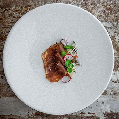 İstanbul’un Michelin Yıldızlı restoranlarından Mikla'ya ait bu görselde, beyaz ve dokulu bir tabağın üzerinde ustalıkla dilimlenmiş füme etler, canlı yeşillikler, ince turp dilimleri ve beyaz bir sos ile özenle hazırlanmış, sade ama derin lezzetler vadeden bir başlangıç sunumu göz alıcı bir şekilde yer alıyor.