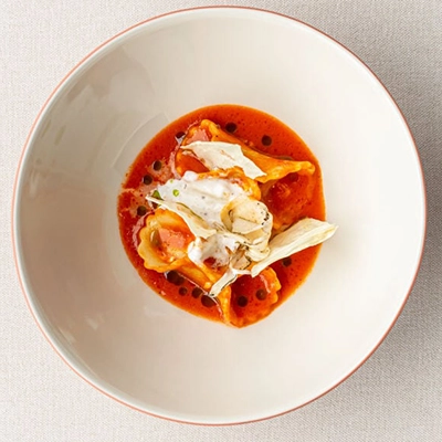 Nicole Restaurant'ın Michelin Yıldızlı restoran kategorisindeki modern Türk mutfağı yorumunu yansıtan bu özel tabakta, kırmızı sosla çevrili, içinde dolgulu hamur işleri bulunan, üzerinde kremalı sos ve incecik sebze dilimleriyle süslenmiş zarif bir yemek sunumu görülüyor, bu lezzetlerin zirvesindeki adreslerden birini temsil ediyor.