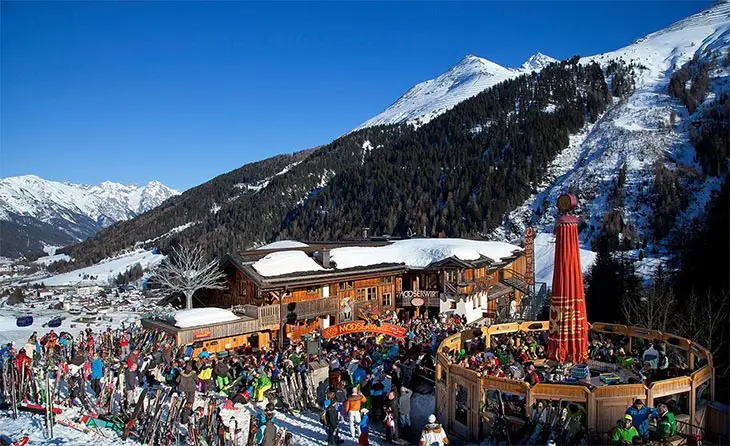 Avusturya St. Anton’da MooserWirt apres-ski barında kalabalık kayakçı grupları ve pist manzarası