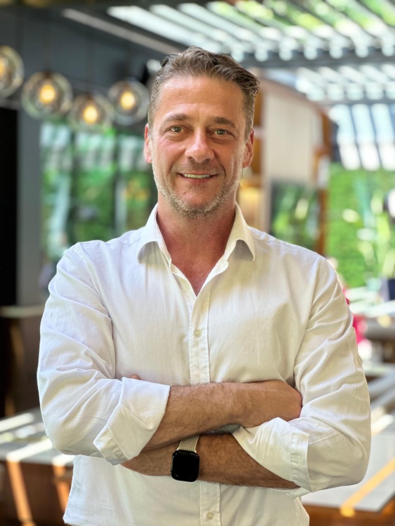 Uzm. Dr. Yıldıray Tanrıver, Infinity Regenerative Clinic Medikal Direktörü olarak, bağışıklık sistemini güçlendirmenin önemli bir yolu olan mikrobiyota dengesi hakkındaki uzman görüşünü paylaşırken, beyaz gömlekli ve kolları kavuşturmuş bir şekilde kameraya gülümsüyor.