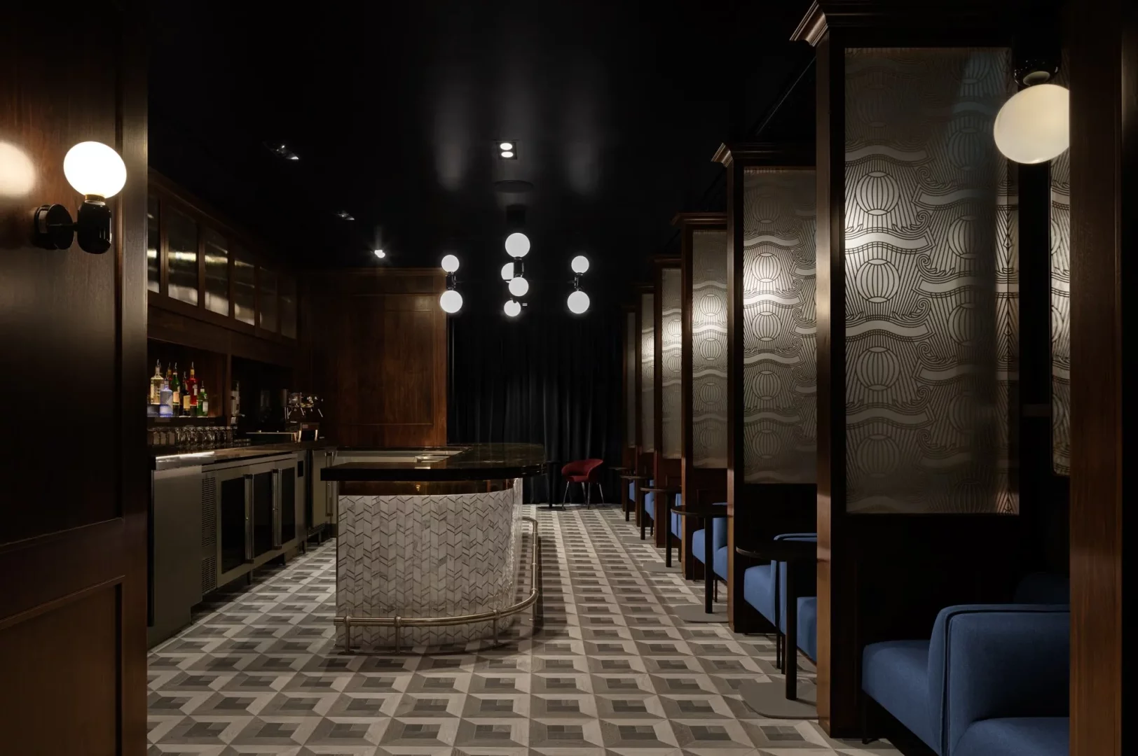 Bu Centurion Lounge Terminal 4 görüntüsünde, şık geometrik desenli zemine sahip lüks bir iç mekan, sol tarafta dolu bir bar alanı, sağda dekoratif bölmelerle ayrılmış mavi koltuklu oturma alanları ve tavandan sarkan yuvarlak aydınlatmalarla modern ve davetkar bir atmosfer sunuluyor.