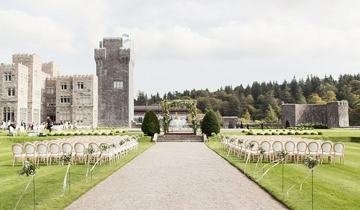 İrlanda’daki Ashford Castle’ın geniş çim alanında kurulmuş açık hava düğün alanı ve arka planda tarihî taş şato mimarisi.
