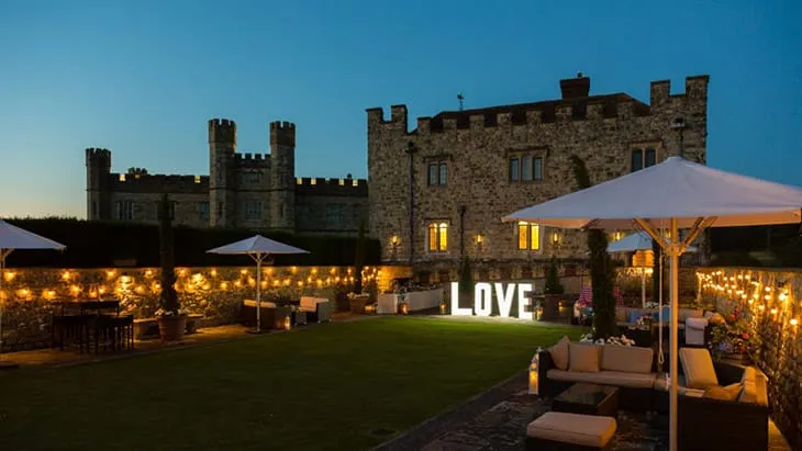 İngiltere’deki tarihi Leeds Castle’ın büyüleyici bahçesinde, loş ışıklar ve dev LOVE tabelası eşliğinde romantik bir gece düğünü atmosferi.