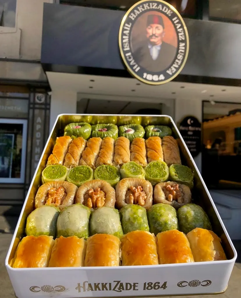 Tarihi Hafız Mustafa 1864 tabelası önünde sergilenen Hakkızade logolu beyaz metal kutuda; fıstıklı sarma, cevizli ve klasik dilimlerden oluşan, Türk tatlı kültürünün eşsiz lezzetini yansıtan çıtır baklava seçkisi sunuluyor.