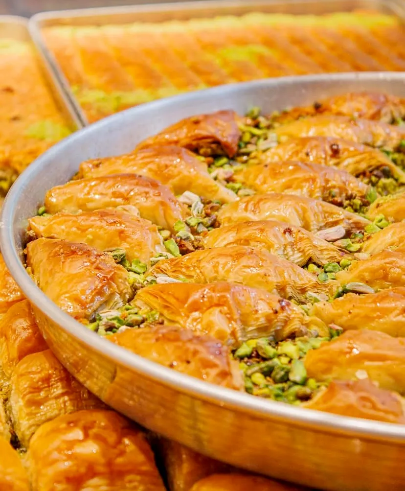 Büyük yuvarlak metal tepside özenle dizilmiş, incecik yufka katmanları arasından yeşil Antep fıstıkları taşan ve altın sarısı şerbetiyle parlayan çıtır midye baklavalar, Türk tatlı kültürünün eşsiz mirasını iştah açıcı biçimde sunuyor.