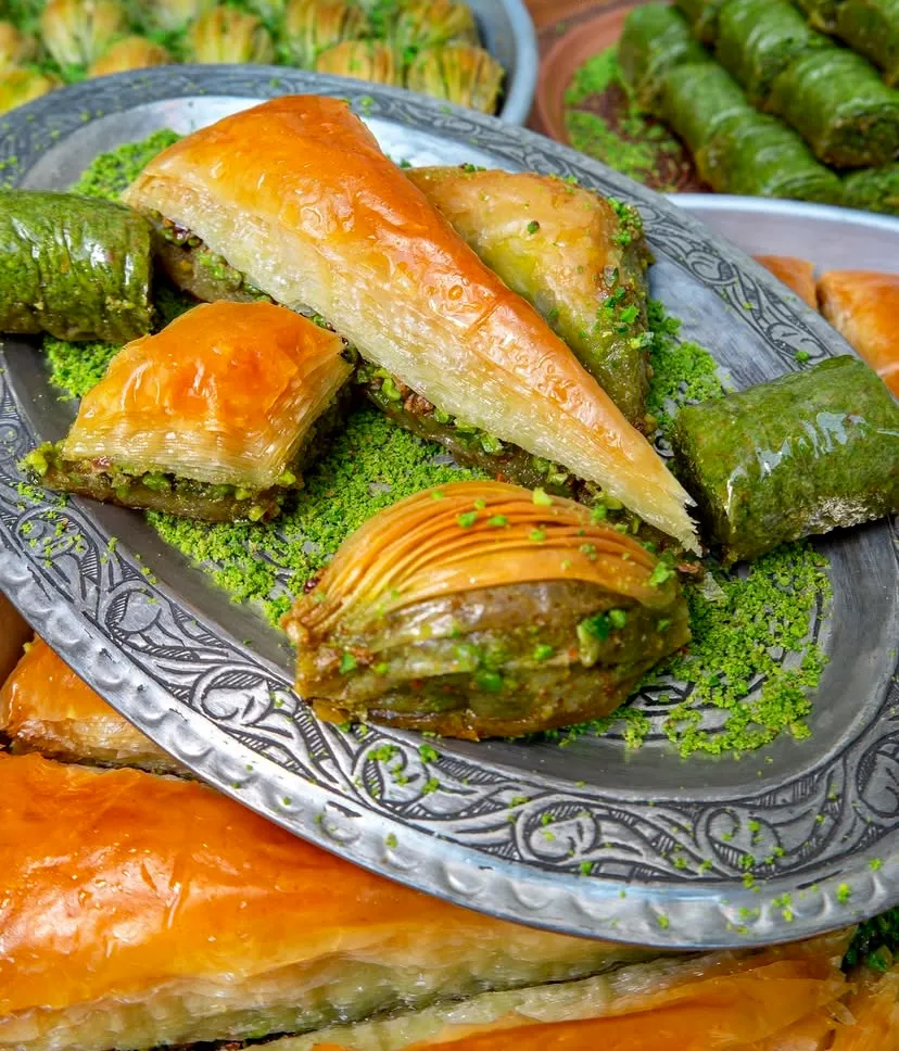 İşlemeli gümüş tepside sergilenen, şerbeti parlayan çıtır havuç dilimi, fıstıklı midye, klasik kare ve yemyeşil fıstıklı dürüm baklavalar. Toz Antep fıstığıyla süslenen bu tatlılar, asırlık Türk mutfağının eşsiz lezzet mirasını