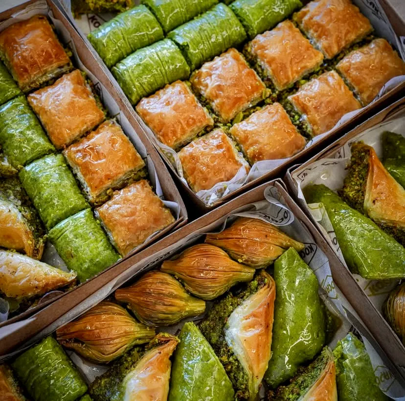 Koçak ambalajlı kutulara dizilmiş altın sarısı çıtır klasik baklava, yemyeşil fıstık sarma, midye ve şöbiyet çeşitleri. Bol fıstıklı ve şerbetli bu tatlılar, köklü Türk tatlı geleneğinin lezzetini ve ustalığını