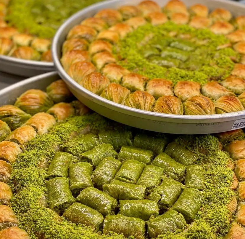 Yuvarlak metal tepsilerde dizilmiş, dışı çıtır yufkalı midye baklavalarla çevrili, ortası yoğun Antep fıstığı ve yemyeşil fıstıklı dürüm dolgulu enfes tatlılar. Türk tatlı geleneğinin ustalığını yansıtan, zengin dokulu ve iştah açıcı bir