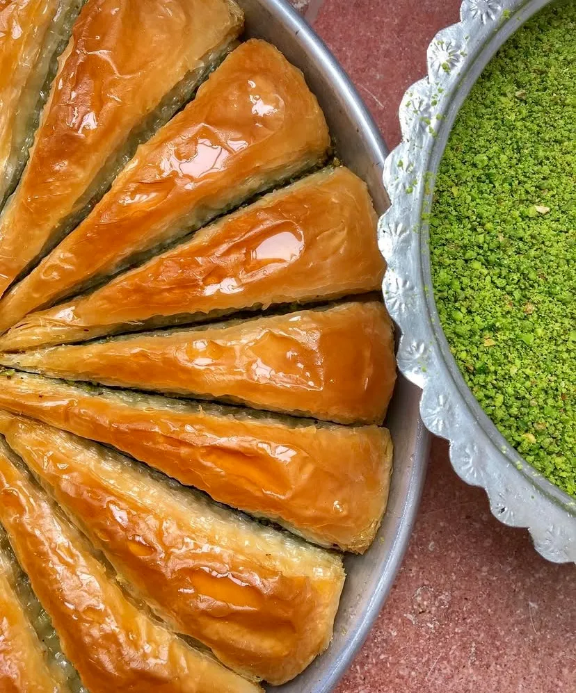 Metal tepside altın sarısı şerbetiyle parlayan üçgen kesim havuç dilimi baklavalar göz alıyor. Yanındaki gümüş kasede dolup taşan yemyeşil çekilmiş Antep fıstığı, geleneksel Türk tatlı kültürünün kusursuz çıtırlığını ve lezzetini temsil