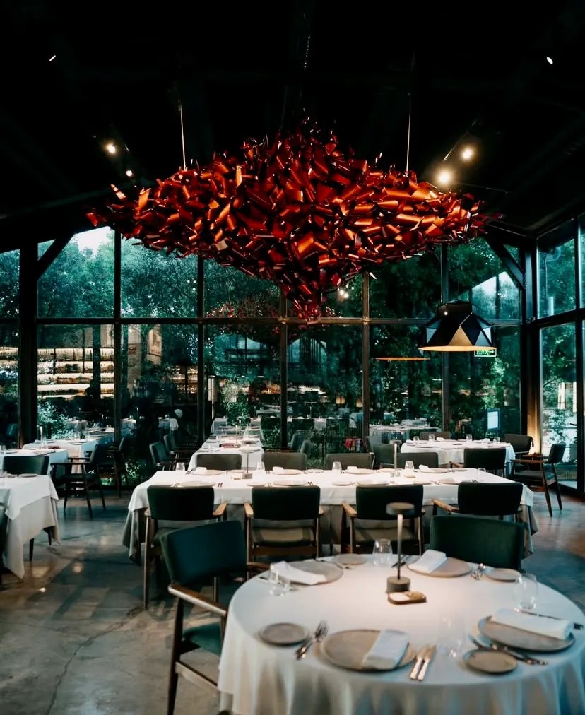 Od Urla restoranının camlarla çevrili şık iç mekânı, beyaz örtülü yuvarlak masalar ve dikkat çekici modern avize ile fine dining atmosferi