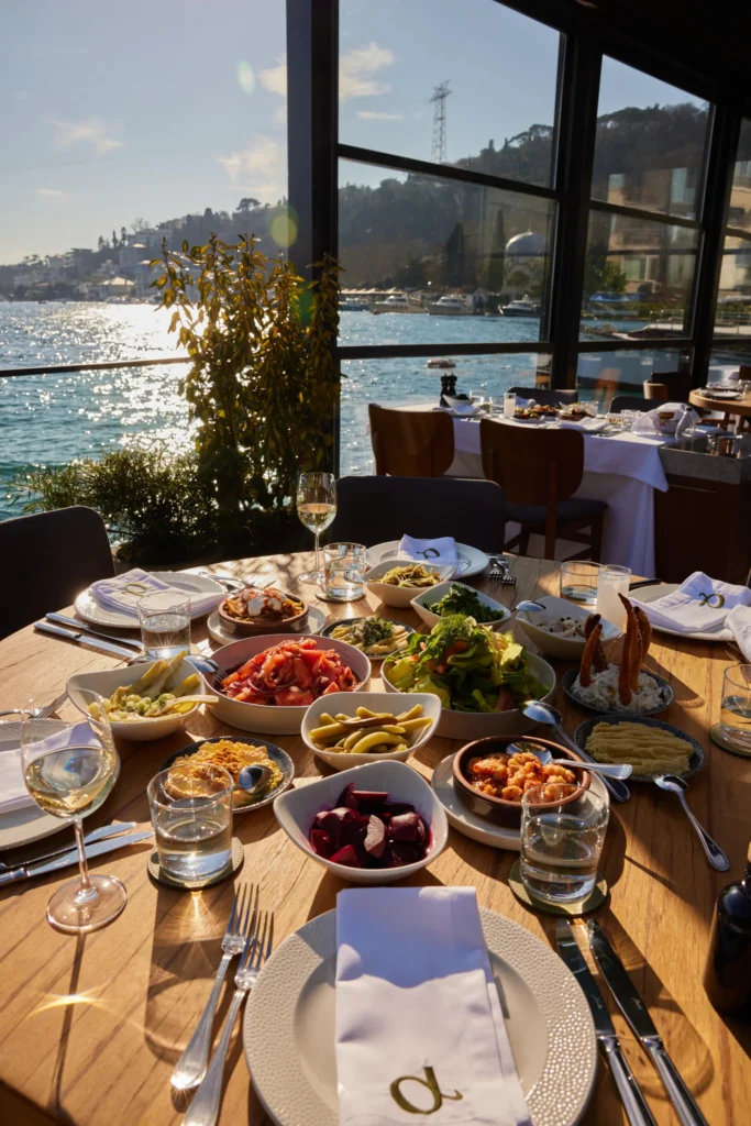 Bebek'in en iyi mekanlarından Paraliaki'de, Boğaz'ın güneşli suları üzerinde parlayan manzaraya karşı kurulan, Akdeniz mutfağının taze ve iştah açıcı mezeleriyle dolu şık ahşap masada, kadehlerde beyaz şarap göz kırpıyor.