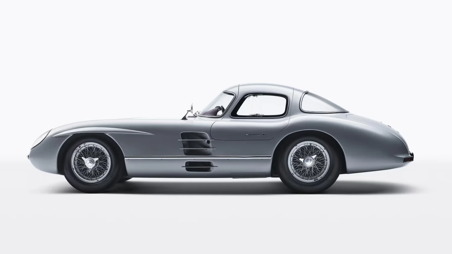 Beyaz bir arka plan üzerinde, dünyanın en pahalı arabası olarak bilinen gümüş renkli, zarif ve aerodinamik tasarıma sahip klasik bir Mercedes-Benz 300 SLR Uhlenhaut Coupe yandan çekilmiş tam görüntüsü.