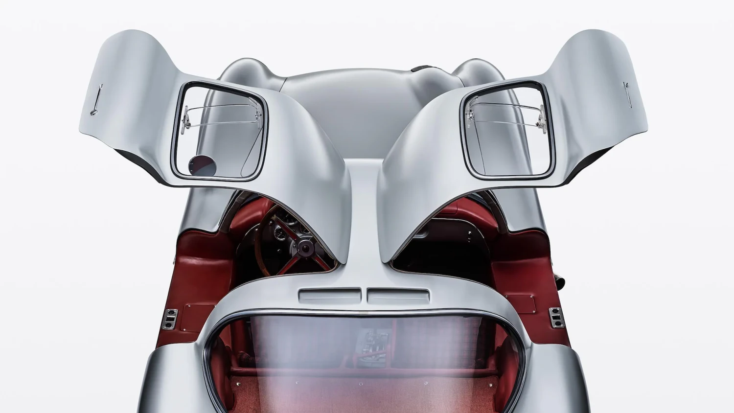 Yukarı doğru açılmış martı kapılarıyla dikkat çeken, gümüş rengi Mercedes-Benz 300 SLR Uhlenhaut Coupé'nin kırmızı deri iç döşemesi ve direksiyonu görünen bir üstten görünümü, bu eşsiz aracın dünyanın en pahalı otomobili olduğunu vurguluyor.