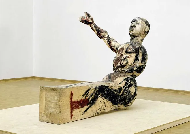Alman ressam ve heykeltıraş Georg Baselitz'in kendine özgü üslubunu yansıtan bu heykel, beyaz, siyah ve kırmızımsı tonlarda, ham fırça darbeleriyle boyanmış, bir blok üzerinde oturan ve kolunu dramatik bir şekilde yukarı uzatmış insan figürüyle, izleyicinin algısını zorlayan provokatif eserleri arasında yer alıyor.