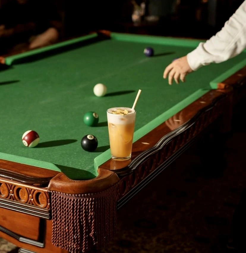 Karloff’ta bilardo masasının kenarında duran kokteyl; arka planda oyuna hazırlanan bir kişi.
