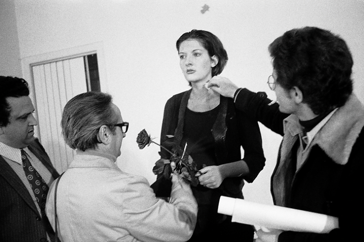 Marina Abramović’in 1974 tarihli Rhythm 0 performansından bir sahne; sanatçı hareketsiz dururken izleyiciler elindeki 72 nesneden bazılarını kullanarak bedenine müdahale ediyor.