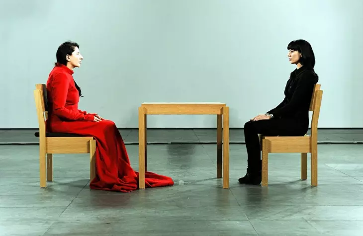 Marina Abramović’in 2010 yılında New York’taki MoMA’da gerçekleştirdiği The Artist Is Present performansından bir sahne; sanatçı, izleyicilerle göz teması kurarak sessizlik içinde derin bir duygusal bağ kuruyor.