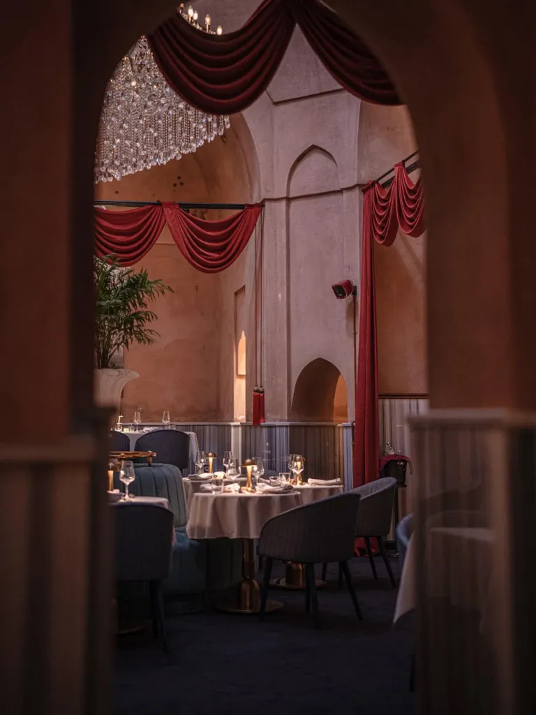 Kırmızı ışıklarla aydınlatılmış loş bir ortamda konumlanan yuvarlak masalar ve şık dekorasyonuyla Olden 1545 Restaurant.